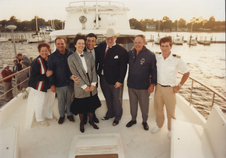 Film photograph of commodores posing for a photo on the deck of a white yacht.